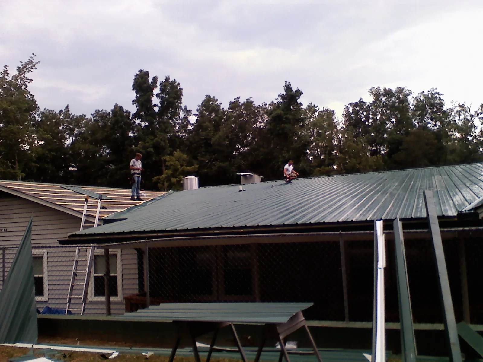 Two roofers installing green metal panels above a covered porch in Douglas