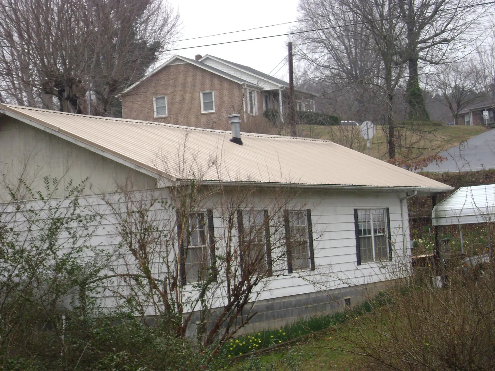 Tan metal roof on a white sided house set into a hillside — Commercial Roofing by Roofing Brothers in Douglas